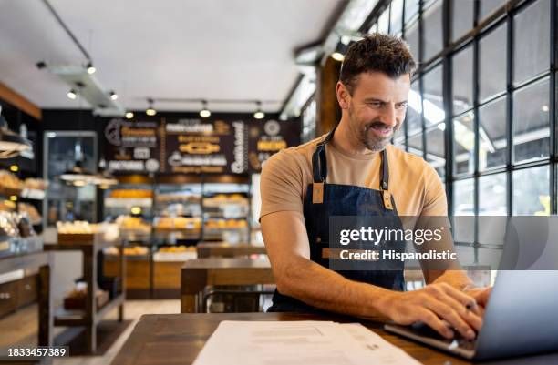 En restaurantejer i forklæde arbejder på sin bærbare computer ved et bord.